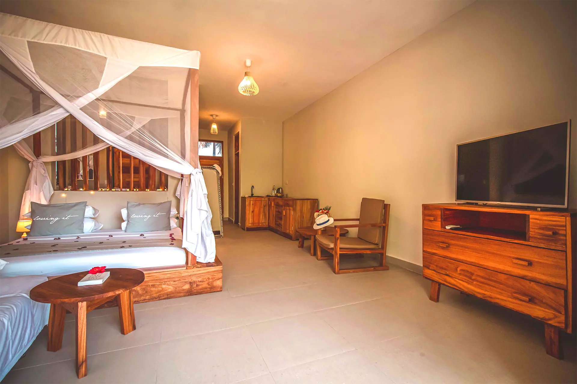 Luksusowy pokój hotelowy na Zanzibarze z dużym łóżkiem z baldachimem, aneksem kuchennym, drewnianymi meblami i telewizorem.
