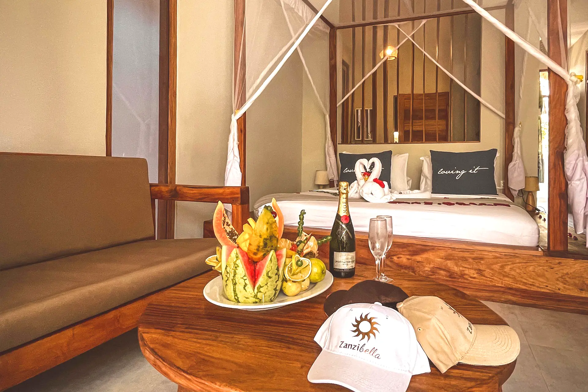 Stolik w eleganckim pokoju hotelowym, na którym znajduje się talerz egzotycznych owoców, szampan i kieliszki.