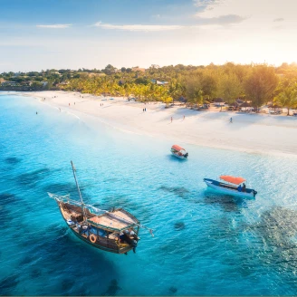 Widok na wybrzeże Zanzibaru – po piaszczystej plaży chodzą ludzie, a w krystalicznie czystej wodzie oceanu pływają łodzie.