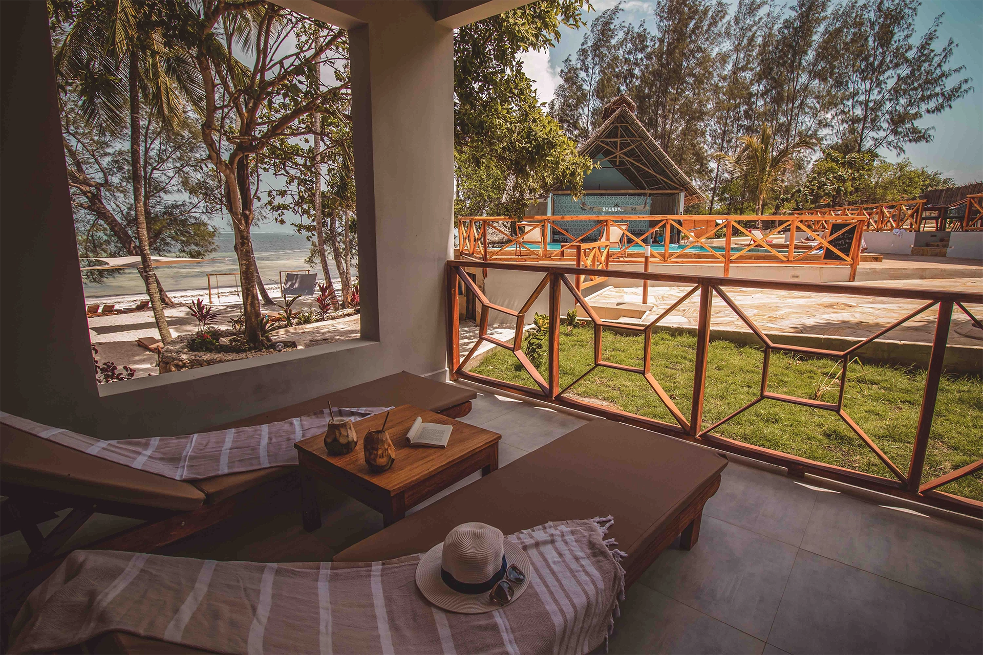 Taras z widokiem na ocean i piaszczystą plażę, z dwoma leżakami i stolikiem z drinkami podanymi w łupinach od kokosa.