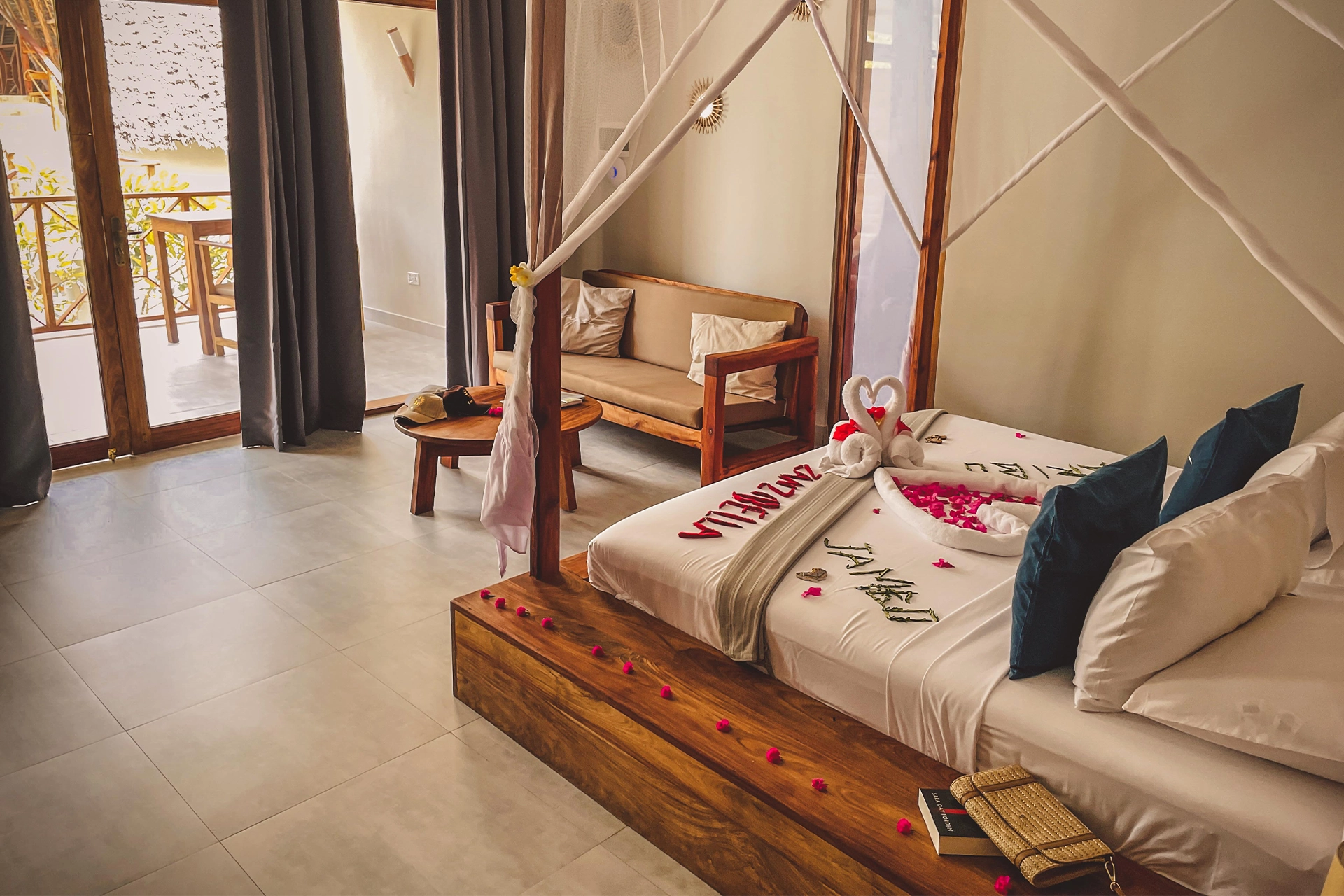 Pokój hotelowy z drewnianymi meblami – wygodną kanapą, stolikiem kawowym i ogromnym, przyozdobionym kwiatami łóżkiem.