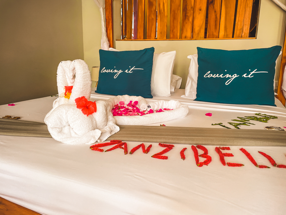 Zaścielone i udekorowane kwiatami łóżko w Zanzibella Hotel&SPA, na którym dwa łabędzie z ręczników kąpielowych tworzą kształt serca.